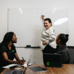 Team meeting with three professionals collaborating around a table and discussing ideas on a whiteboard.